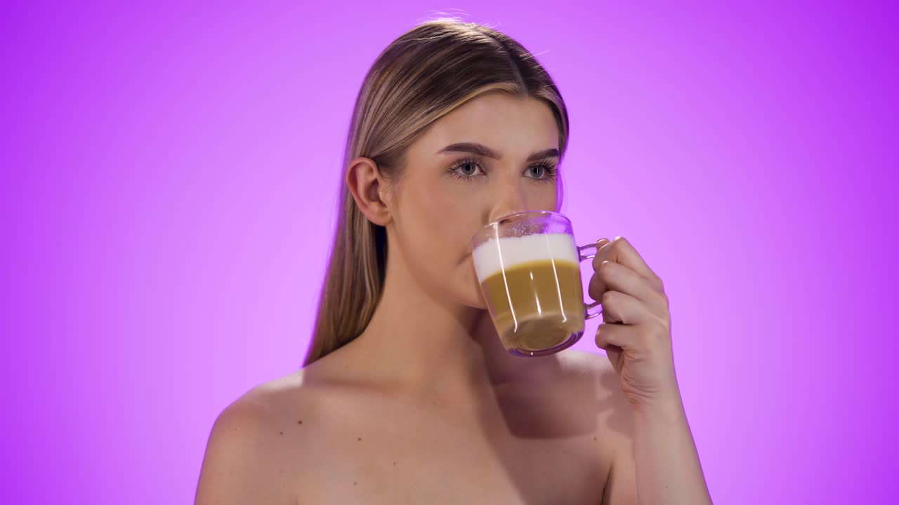 primer plano medio de una mujer joven y bonita mientras disfruta de un café latte machiato o capuchino recién preparado con leche de avena vegana y disfruta del buen sabor frente a un fondo púrpura en cámara lenta