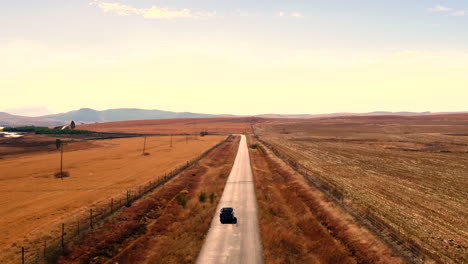 Alto-Dron-Subiendo-Tiro-Detrás-De-Un-Automóvil-Vintage-Black-Austin-Westminster-Conduciendo-A-Través-De-Las-Colinas-De-Sudáfrica-Durante-El-Invierno-Seco-4k