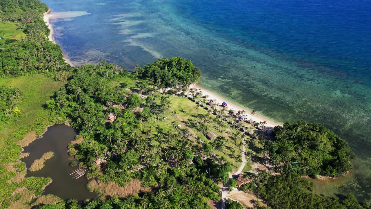 Panoramic aerial drone shot of vibrant white sand coastal resort amid lush jungles and turquoise ocean waters at Yocti, Catanduanes, Philippines.