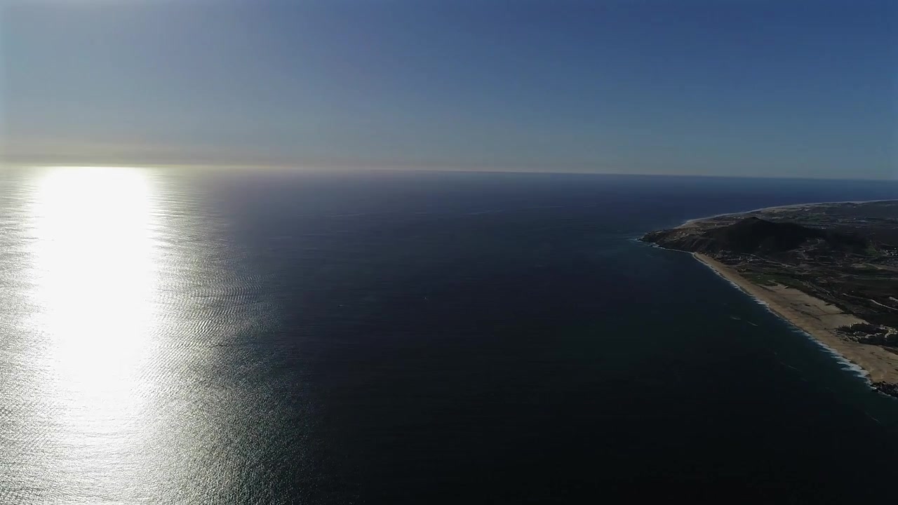 Drone vola alto sull'Oceano Pacifico, partendo sopra la costa settentrionale di Cabo San Lucas e la comunità di Quivira, con una panoramica sull'acqua che rivela il sole prima di terminare con una vista aperta.