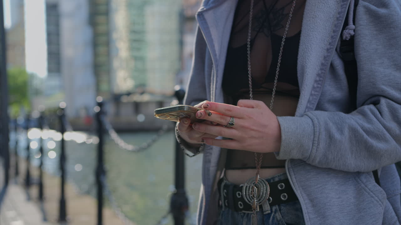 fotografía de cerca de un estilo alternativo de una mujer enviando mensajes por teléfono móvil fumando un cigarrillo enrollado a mano al aire libre - tomada en tiempo real