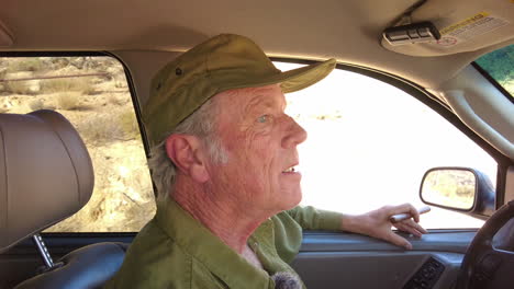 Aged-handsome-male-inside-car-drives-in-reverse-while-holding-cigar