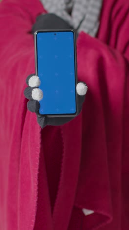 Vertical-Video-Close-Up-Of-Cold-Person-Wearing-Blanket-Holding-Blue-Screen-Mobile-Phone-Trying-To-Keep-Warm-In-Energy-Crisis