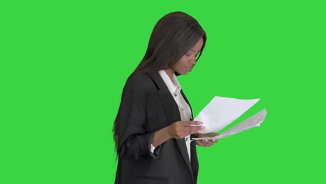 mujer afroamericana seria leyendo documentos mientras camina en una pantalla verde, llave de croma