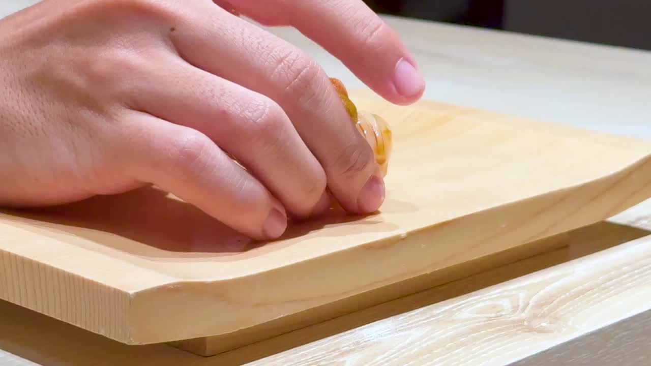 Close-up of hands placing sushi on a wooden board, highlighting the intricate presentation of the dish.