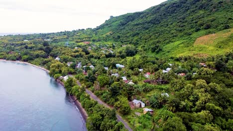 drone aéreo ascendente de las casas de la comunidad costera rural, el paisaje verde montañoso y el océano en la isla de alor, east nusa tenggara, indonesia