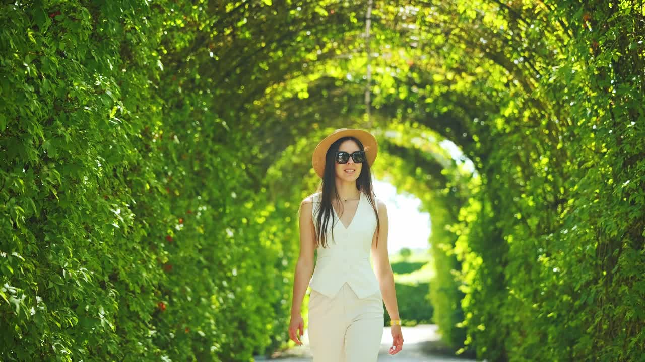 Elegant woman walks toward camera under lush archway with sunbeams glowing