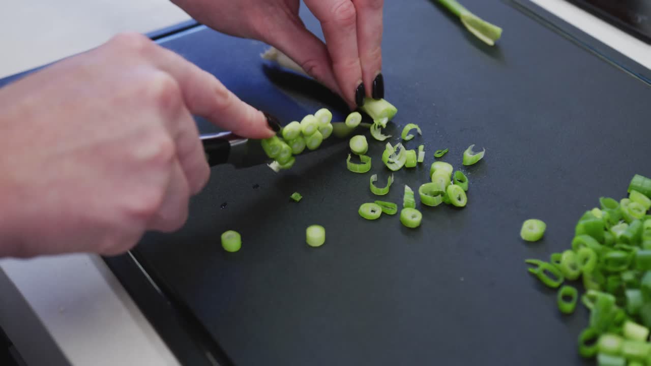 Caucasian female hands slicing spring onions on a cutting board