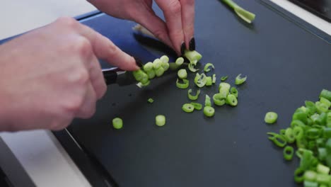 Caucasian-female-hands-slicing-spring-onions-on-a-cutting-board-