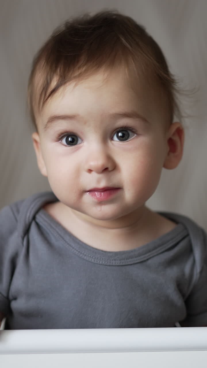 Adorable smiling baby boy standing in white cot swaying a little. Child smiles sweetly showing two lower new teeth. Close up. Vertical video