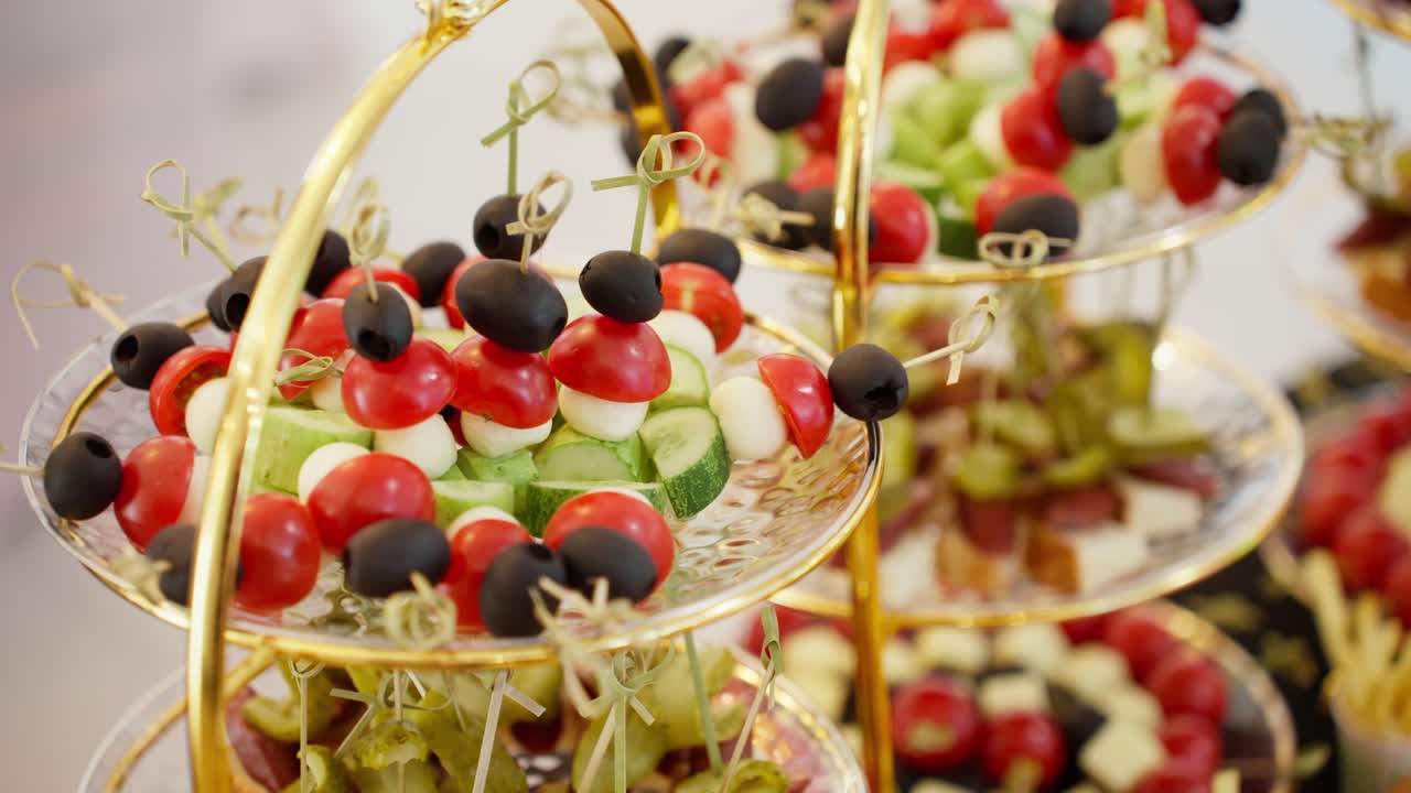 A smooth parallax camera move glides past a beautiful, multi-tiered serving tray displaying fresh, colorful appetizers and canapés at a wedding, party, or corporate event.