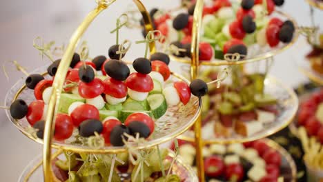 a smooth parallax camera move glides past a beautiful, multi-tiered serving tray displaying fresh, colorful appetizers and canapés at a wedding, party, or corporate event.