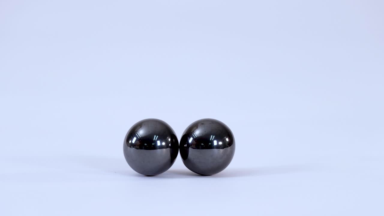 Close-up shot of two metallic magnetic balls rolling together and colliding on white background