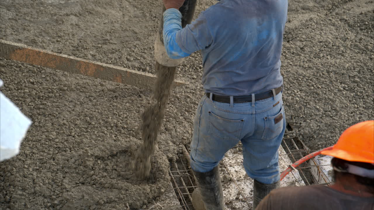 Slow motion close-up of a mexican latin construction worker pouring fresh concrete mix onto a grid to make the slab of a house in Mexico
