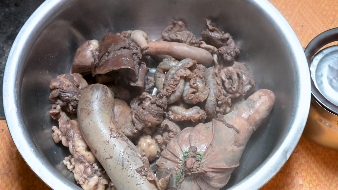 A steaming bowl of freshly cooked sheep offal, a traditional nomadic meal. A close-up on nose-to-tail cuisine, featuring liver, intestines, and meat-filled stomach.