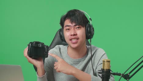 close up of a smiling asian man with computer reviewing camera while sitting in front of green screen background