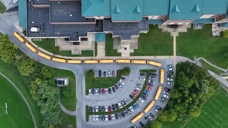 large american high school with line of yellow school buses waiting to pick students up after school day