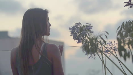 A-young-woman-looks-over-the-glass-railing,-enjoying-the-view-of-the-city-in-the-evening