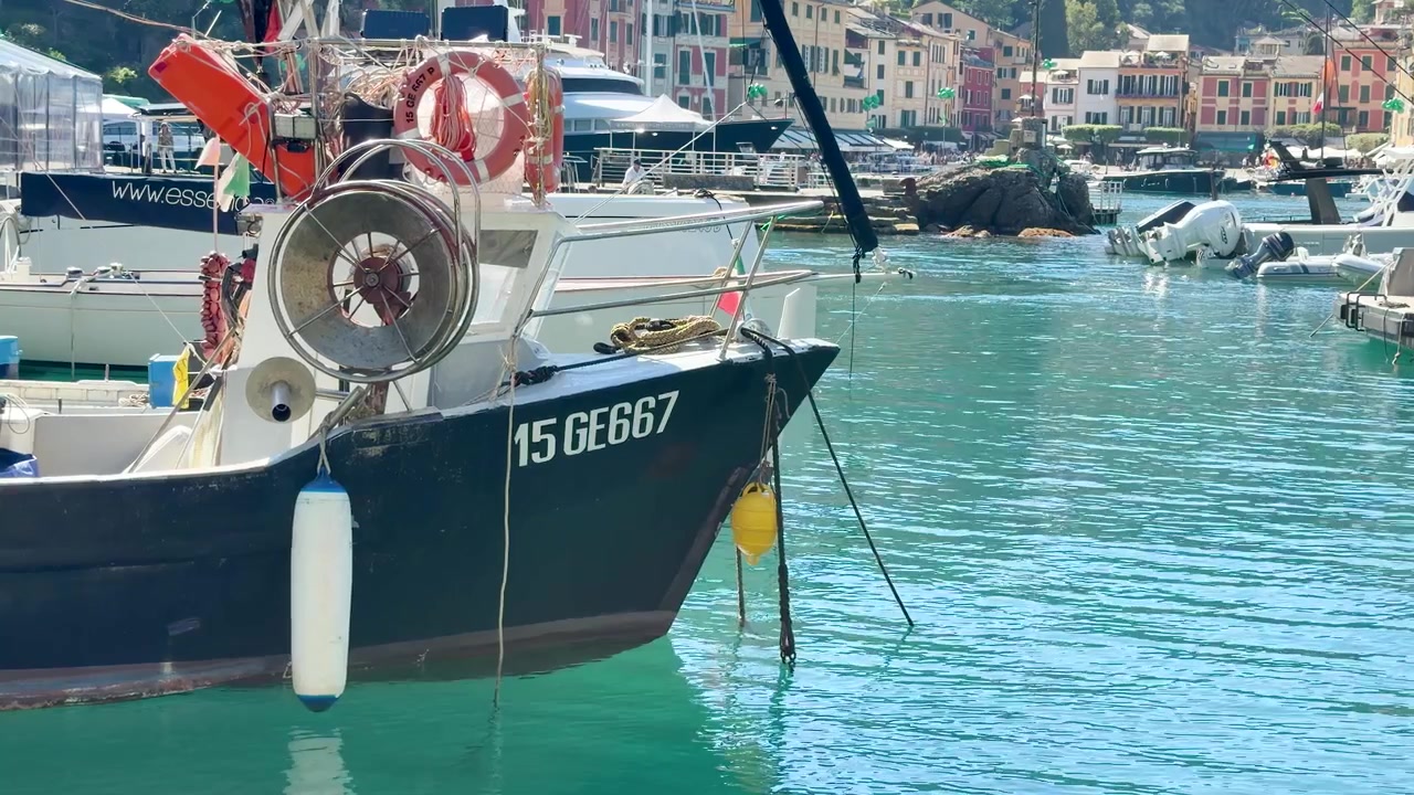 Un'inquadratura statica di una barca da pesca che galleggia su acqua turchese in un porto turistico mediterraneo.