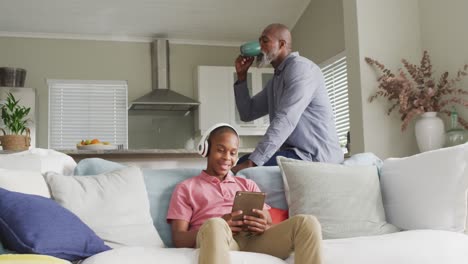 video of happy african american father drinking coffee and watching tablet with son