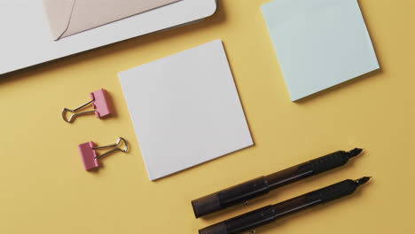 overhead view of notebook, pens and stationery arranged on yellow background, in slow motion