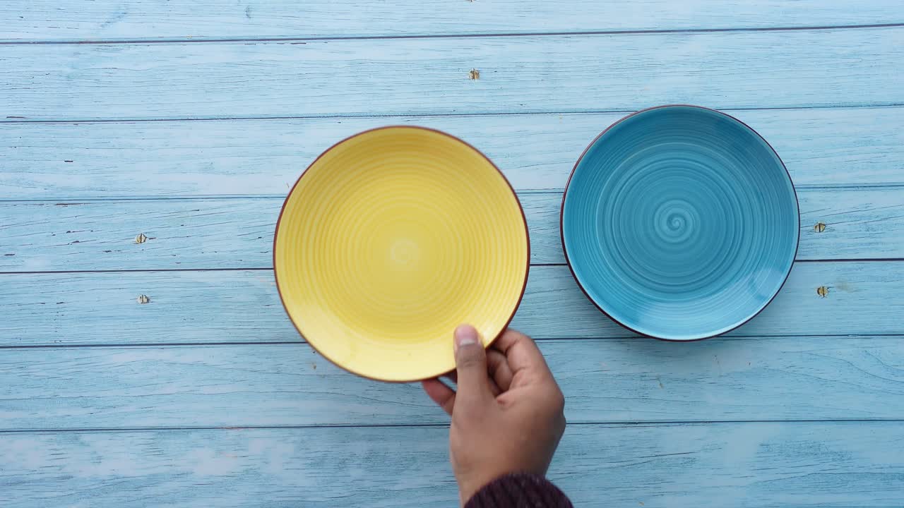 Hand Placing Colorful Plates on a Blue Wooden Table