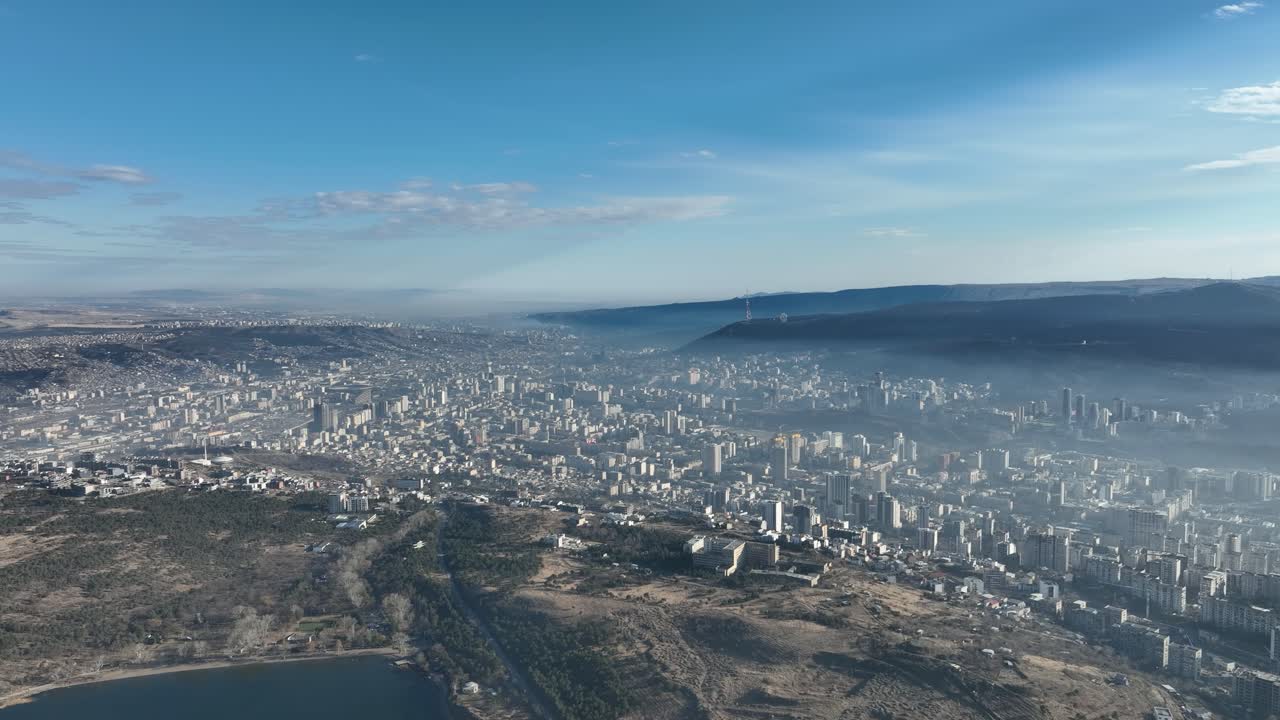 A vast city stretches towards the horizon, with a network of buildings and streets forming an intricate pattern. Distant mountains provide a scenic backdrop to the bustling metropolis