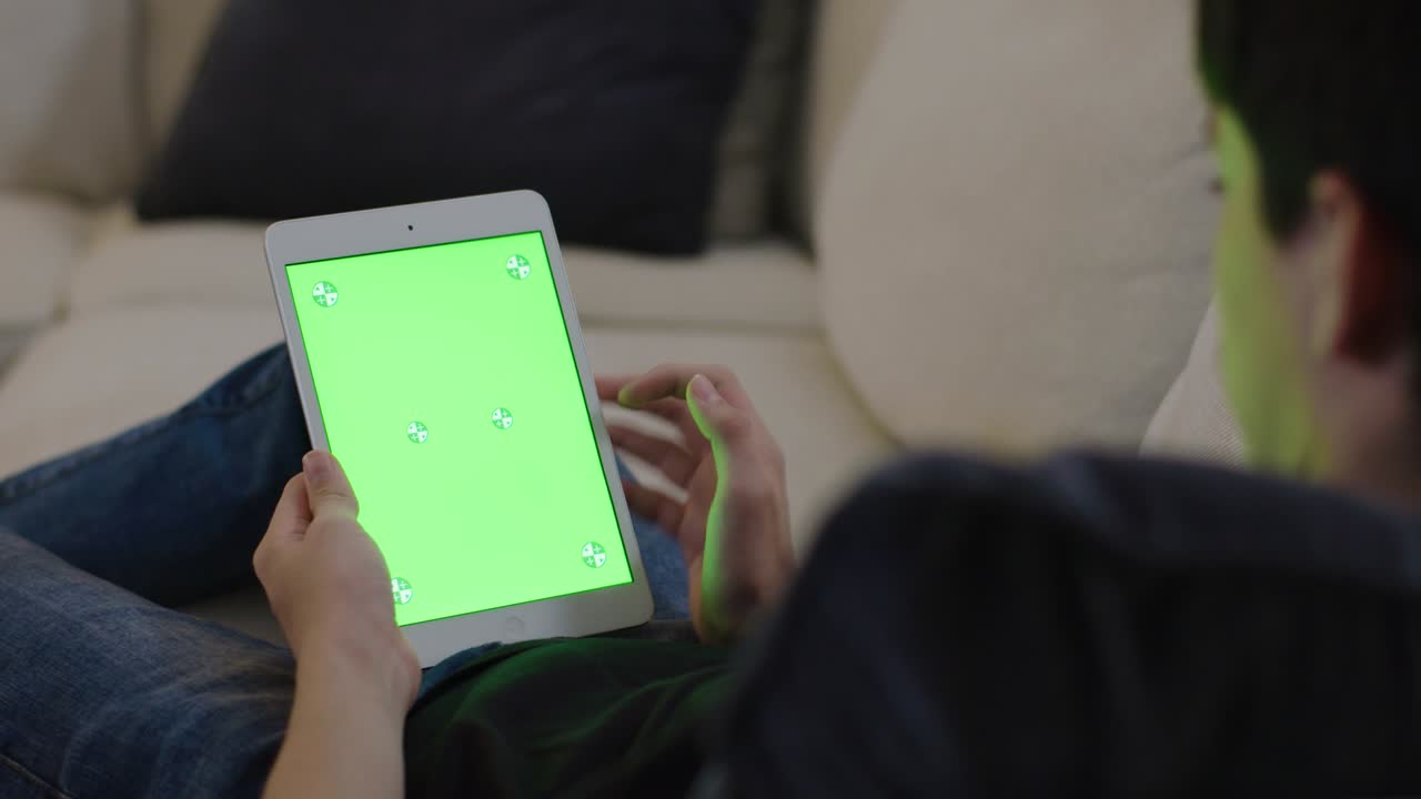 hombre joven sentado en el sofá, adolescente masculino en casa usando un dispositivo móvil para la tarea. tableta monitor de computadora pantalla verde para internet.