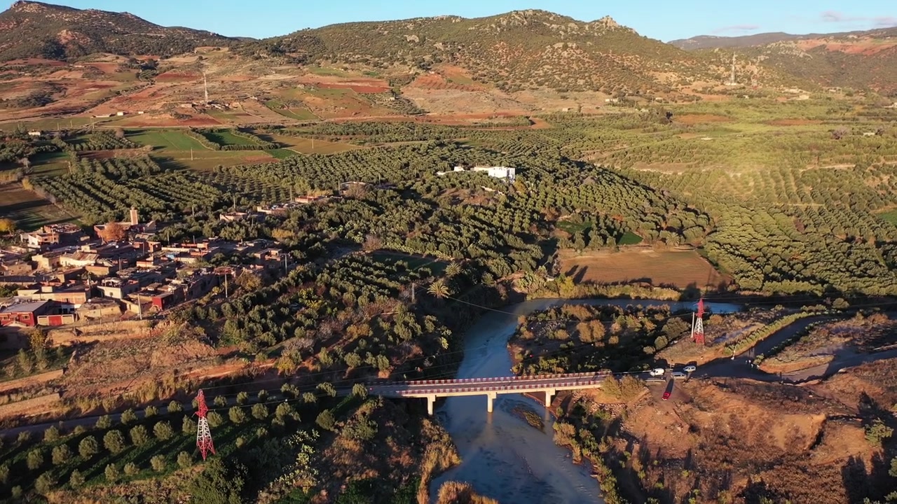 Ampio panorama aereo da drone di una valle rurale con fiume e uliveti durante l'ora d'oro nel Medio Atlante, Marocco, ideale per progetti di viaggio, natura e campagna.