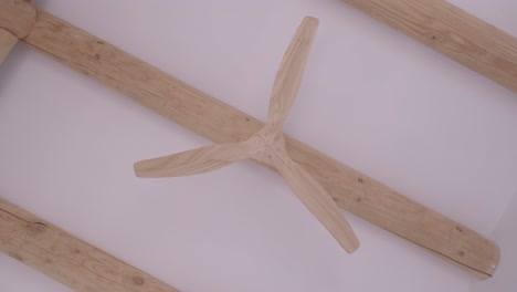 light-wood fan seen from below, on a light-wood beam on a white ceiling