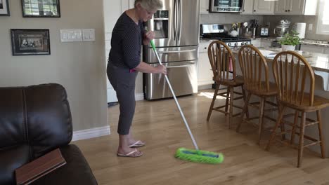 senior woman dusts and sweeps her kitchen floors - tilt up