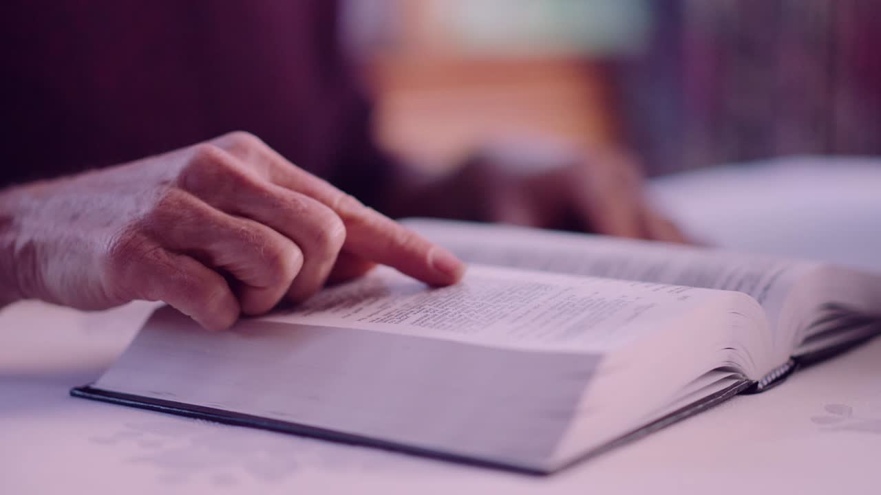 A close up shot shows a hand reading through the bible. The subject is out of the frame as well the blur background.