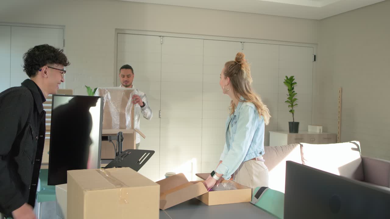 Diversi colleghi che disimballano monitor e rimuovono l'imballaggio a casa dopo che un uomo è entrato per preparare l'installazione