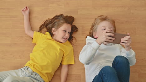 little girl and boy with a smartphone lying on the floor, using an app and playing an online video game