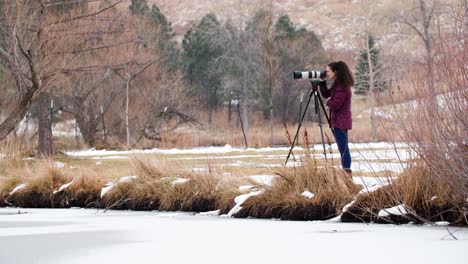 woman photographer taking pictures with camera at frozen lake in colorado park