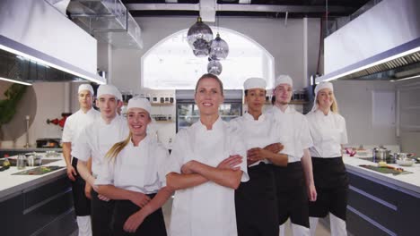 Multi-ethnic-chefs-wearing-chefs-whites-in-a-restaurant-kitchen,-a-mixed-race-male-chef-crossing-his