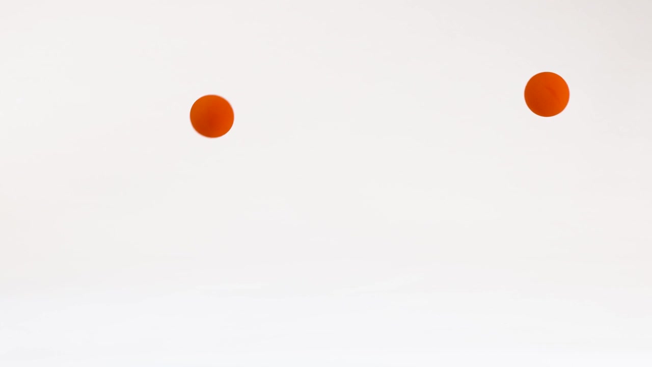 A vibrant orange ball bounces and rolls across a clean white surface with soft lighting