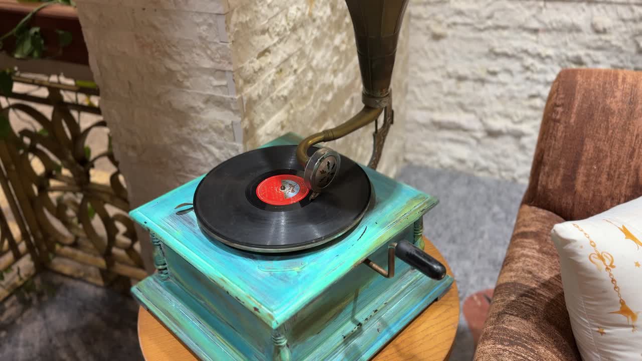 Un grammofono antico che riproduce un disco in vinile su una base di legno turchese, posizionato su un tavolino rotondo accanto a un divano in un accogliente ambiente interno retrò.