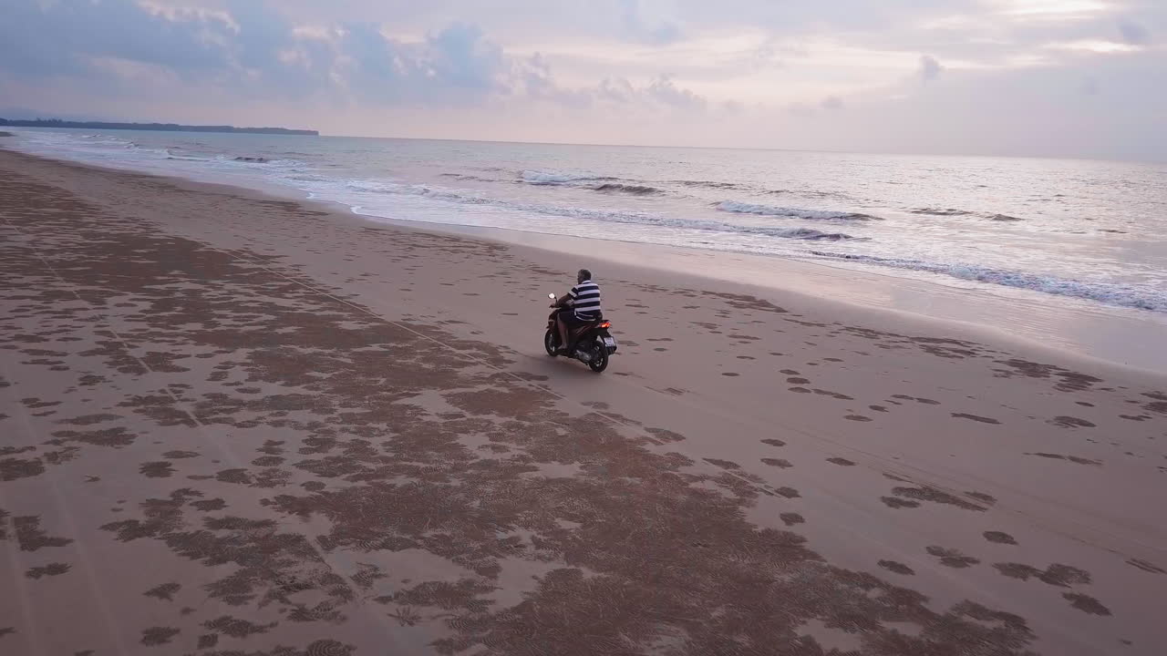 Veduta da drone di una moto che guida sulla spiaggia con il sole che tramonta.