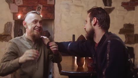 travelers see fellow guy in tavern. drunk man happy to meet stranger while angry companion sits friend down in medieval guesthouse. fantasy performance