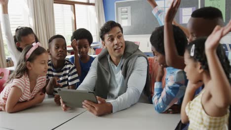 happy diverse male teacher with schoolchildren using tablet in classroom at elementary school