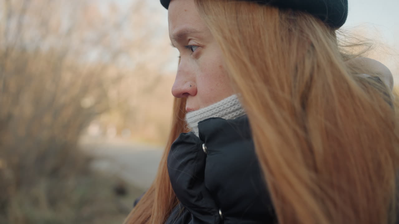 Closeup outdoor portrait woman writing notebook, pensive expression with beanie and puffer jacket, freckles and long red hair, pen tracing sketches and notes, muted winter reeds and soft sunlight
