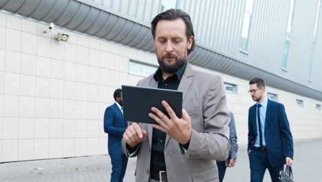 gray-haired businessman in stylish clothes using a tablet in the street