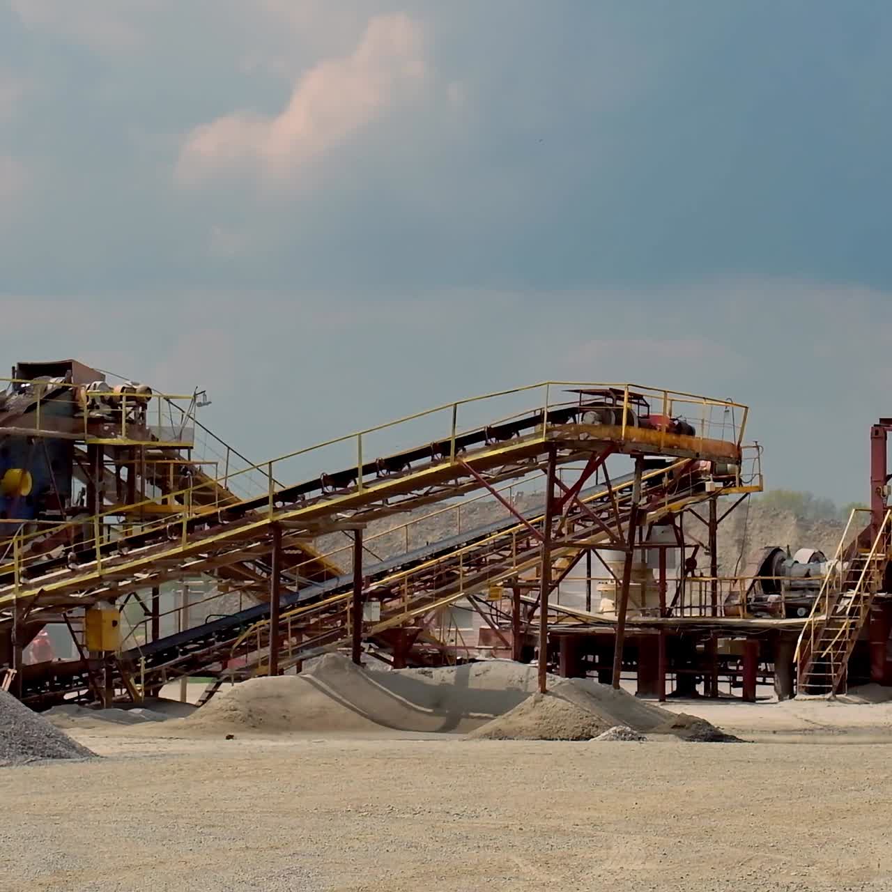 Industrial plant outdoors. Stone crusher machine and piles of gravel under blue sky. Metal equipment for production of building materials.