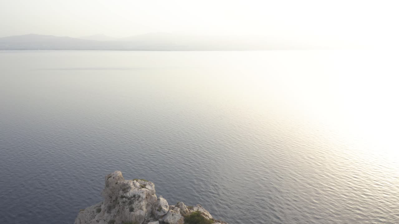 un dron aéreo avanza desde un faro en el borde de unos acantilados hacia el mar