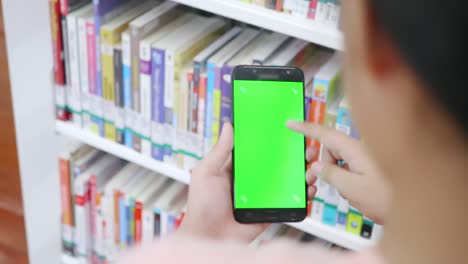 close up hand asian girl holding a green screen on smartphone searching for a book in the library