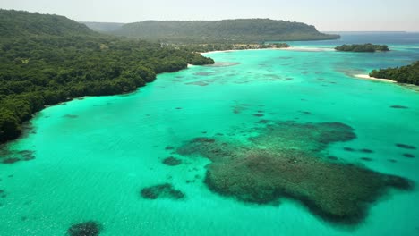 a drone flies over crystal clear waters and the village of port olry on the island of espiritu santo