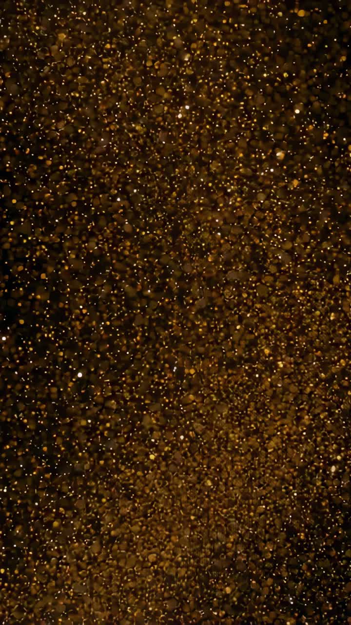 Vertical video: Shifting camera focus revealing gold particles in dark studio and emphasizing bokeh