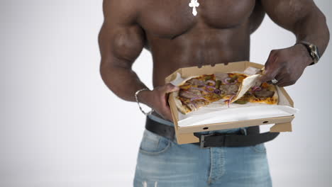 Male torso of african athlete. Young muscular african man with naked torso eating pizza in studio