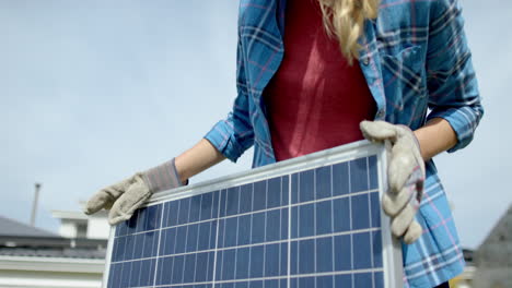 Retrato-De-Una-Mujer-Cauasiana-Feliz-Con-Guantes-Sosteniendo-Un-Panel-Solar-En-El-Jardín,-Cámara-Lenta